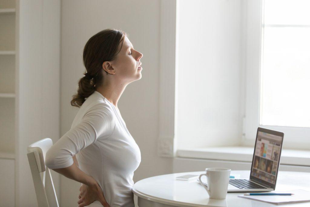 une femme au travail souffre du dos. Elle se soutient les lombaires car elle a une arthrose lombaire.